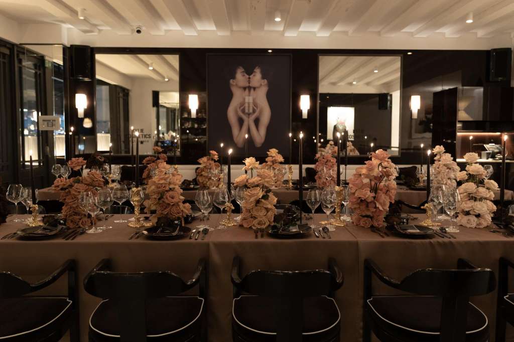 Long banquet table set with peach floral centerpieces, place settings, and glassware against mirrored black walls.