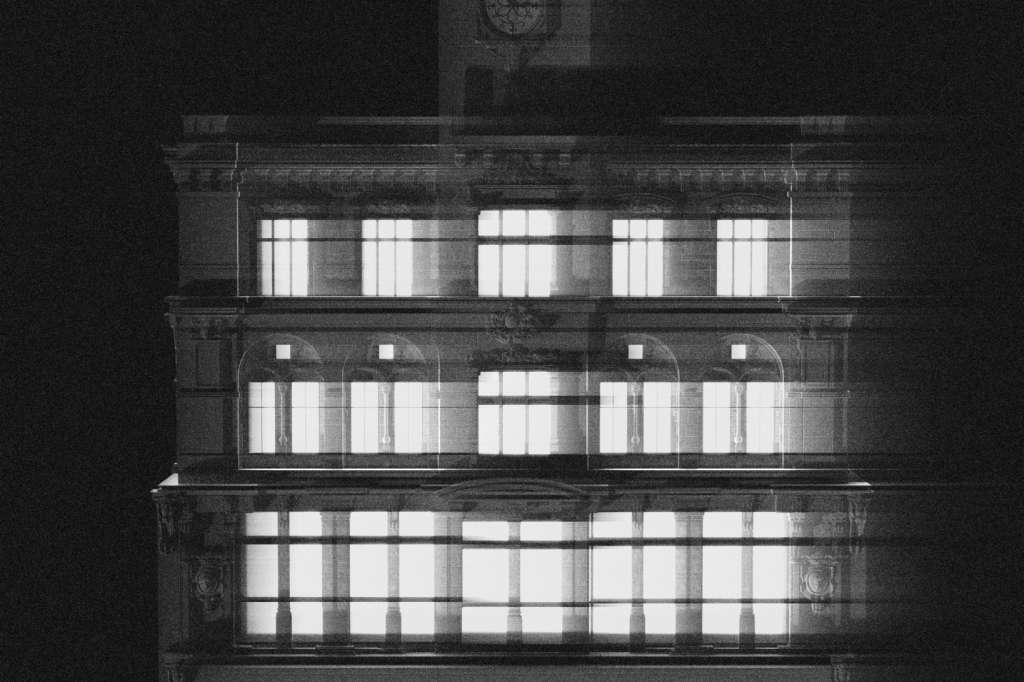 Historic stone building facade at night with illuminated windows and clock tower.