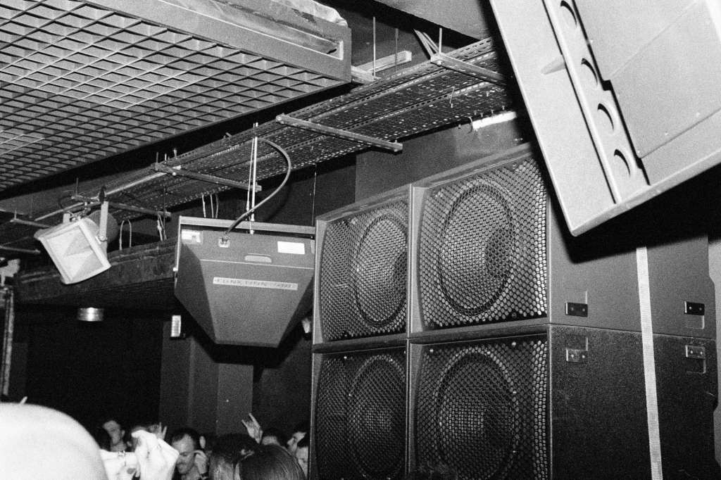 Sound equipment and speaker stack mounted overhead in a venue space with industrial ceiling and metal framework.