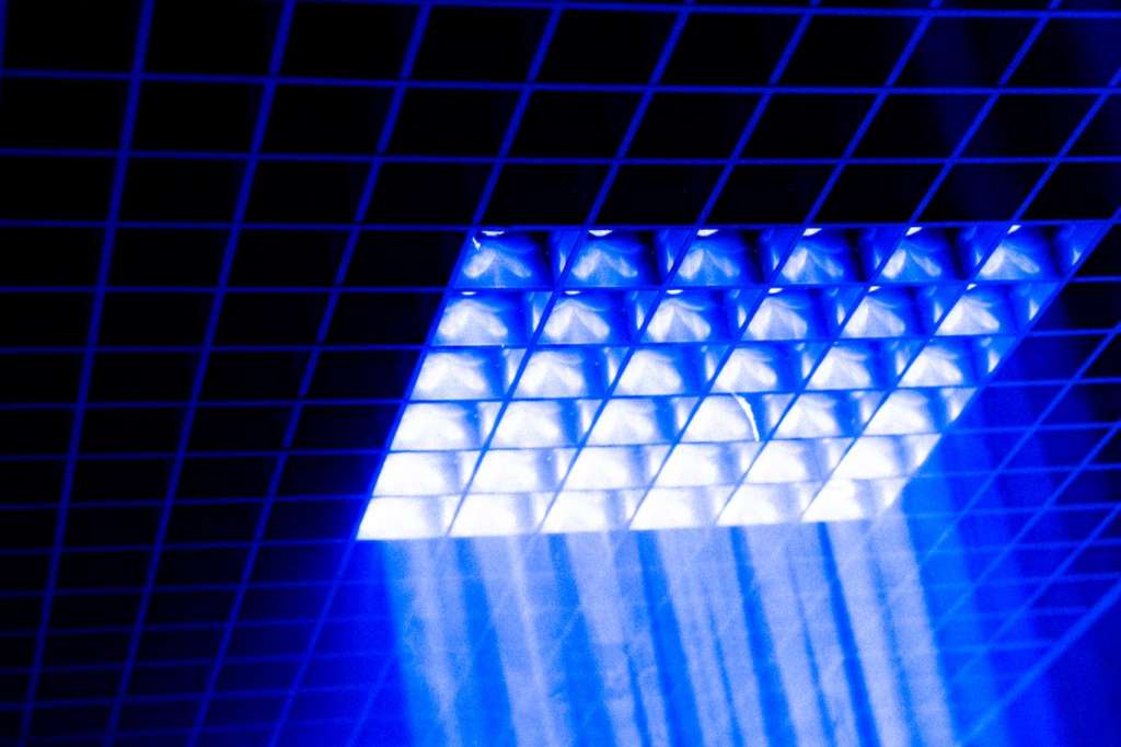 Ceiling grid with blue and white LED lighting creating dramatic geometric patterns and light beams.