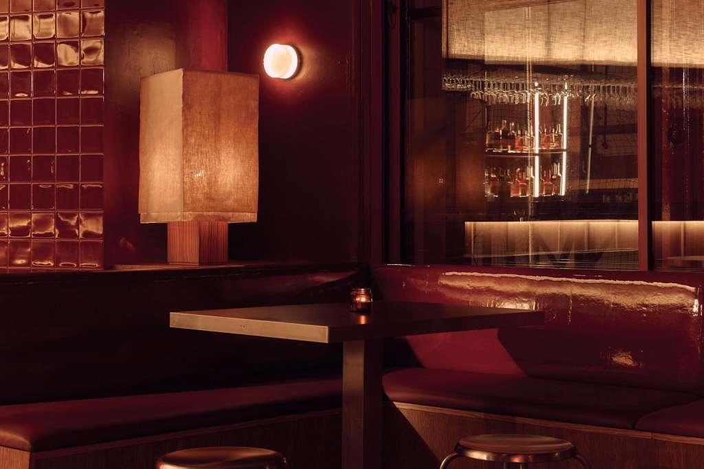 The Club lounge with burgundy seating, ambient warm lighting, decorative wall panels, and bar visible through glass partition.