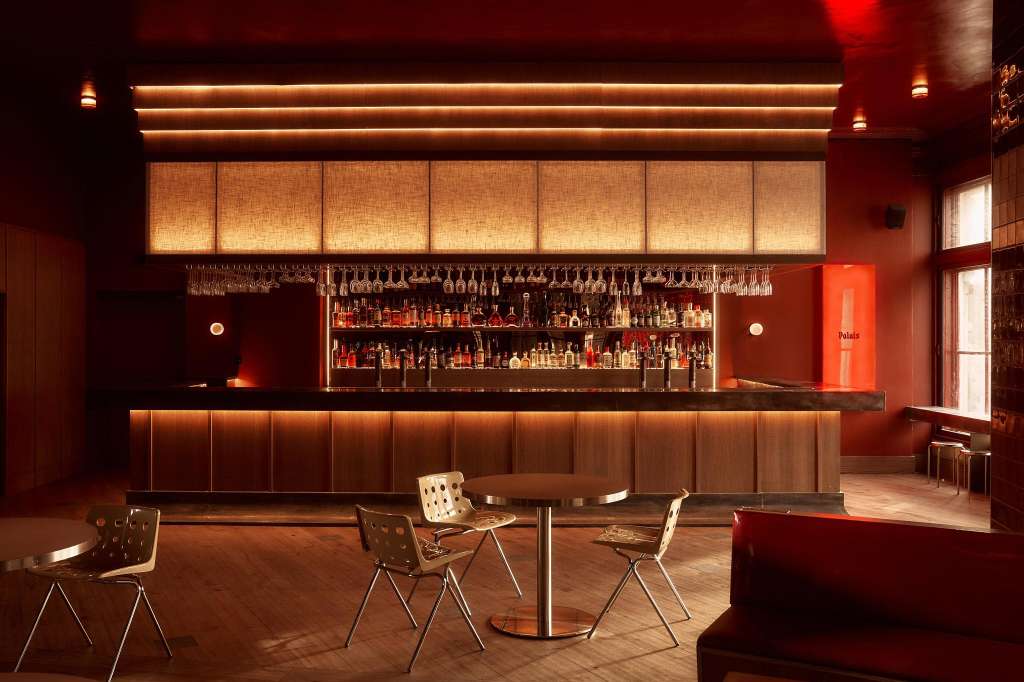 Modern bar lounge with illuminated backlit panels, full liquor shelves, and contemporary seating around small tables.