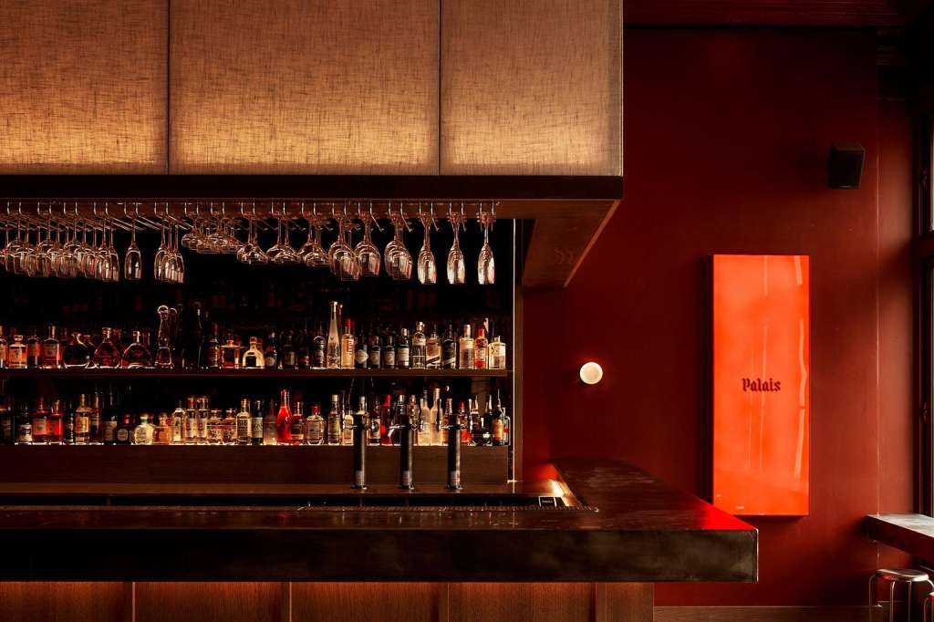 The Club bar area with illuminated shelving, stocked bottles, hanging glassware, and red ambient lighting.