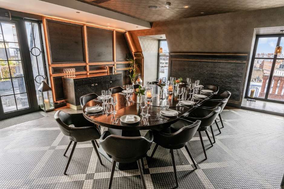 Modern dining room with long black table, place settings, glassware, and black chairs arranged for a seated meal.
