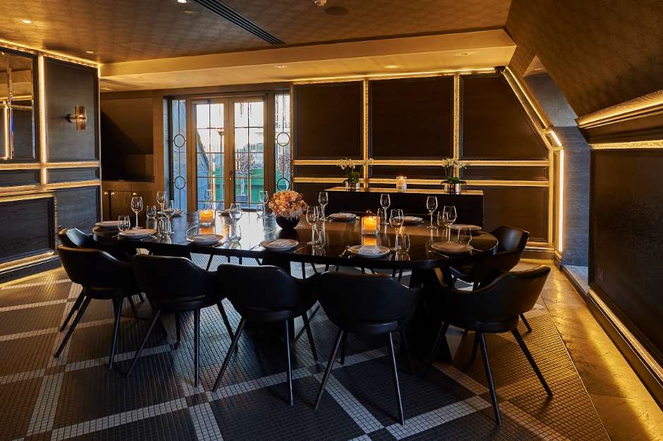 Private dining room with black table, modern chairs, place settings, and gold-trimmed windows overlooking a cityscape.