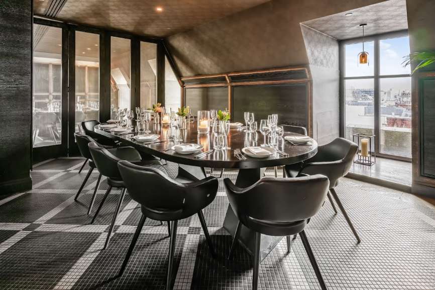 Modern dining room with black oval table, contemporary chairs, place settings, and floor-to-ceiling windows overlooking cityscape.