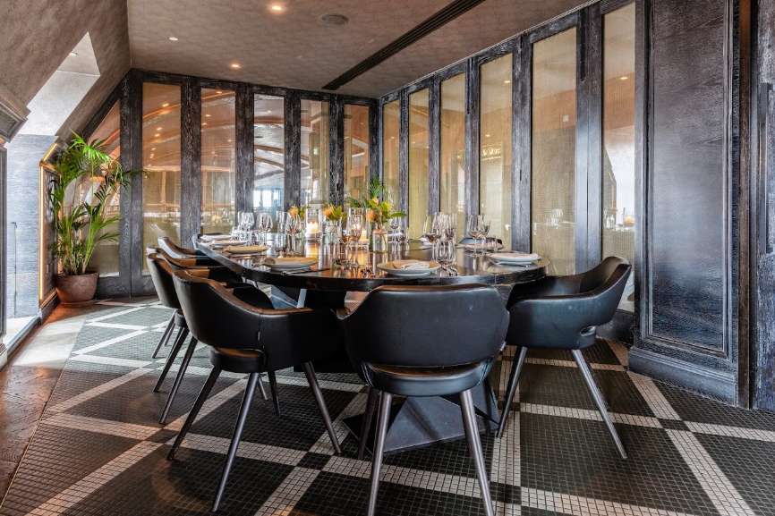Modern dining room with black table, contemporary chairs, place settings, and floor-to-ceiling windows overlooking cityscape.