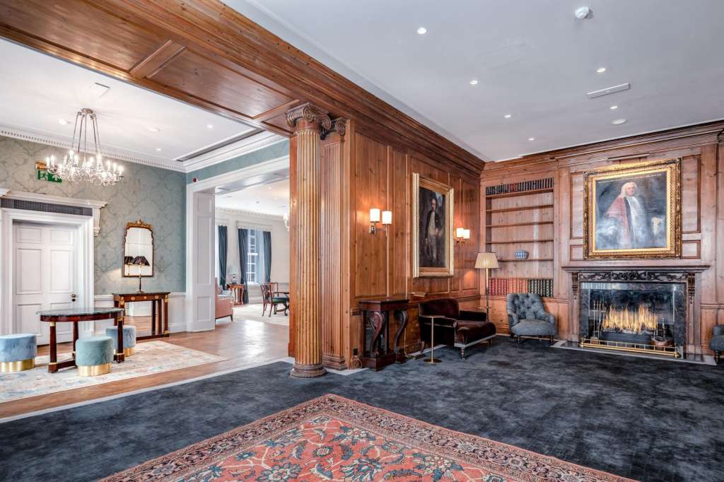 Elegant reception space with wood paneling, fireplace, bookshelves, chandelier, and formal seating areas.