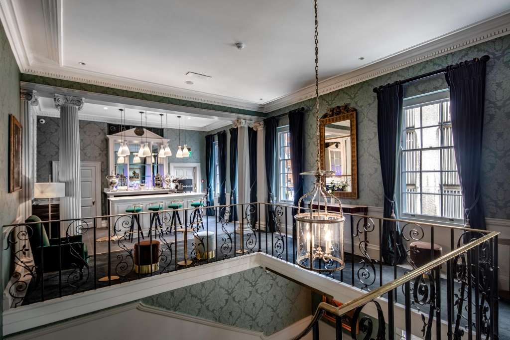 Elegant mezzanine bar area with ornate railings, pendant lighting, mirrored bar counter, and formal furnishings.