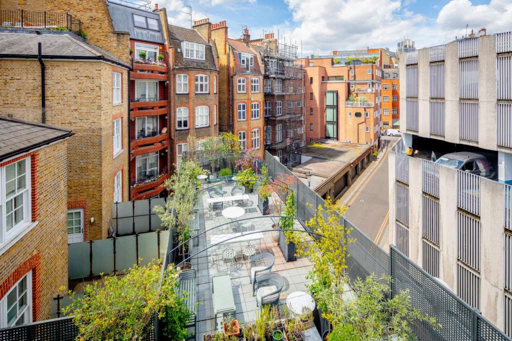 Aerial view of a London courtyard with brick buildings, green foliage, and paved seating area below.