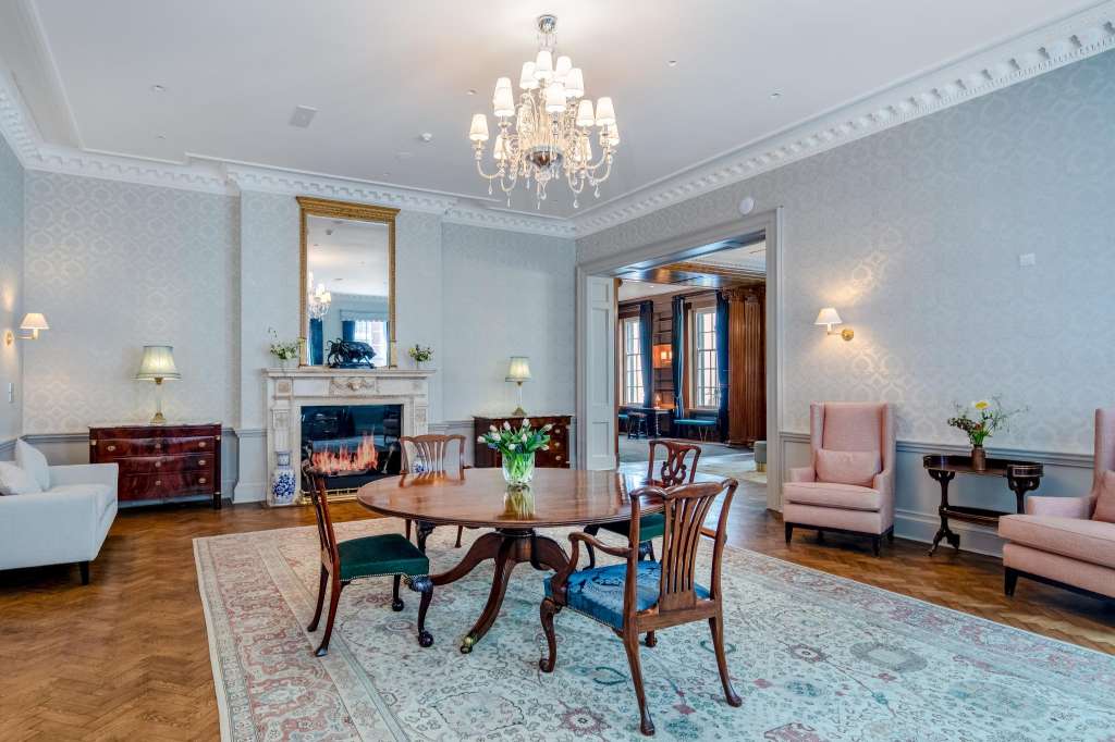 Elegant reception room with fireplace, round dining table, pink armchairs, chandelier, and period furnishings.