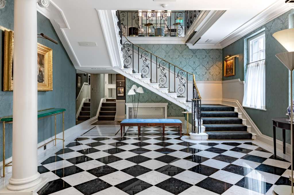 Grand entrance hall with black and white diamond flooring, ornate staircase, teal damask walls, and classical architectural details.