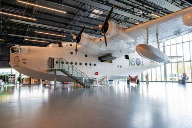 Large vintage aircraft displayed in a hangar with polished concrete floor and industrial ceiling lighting.
