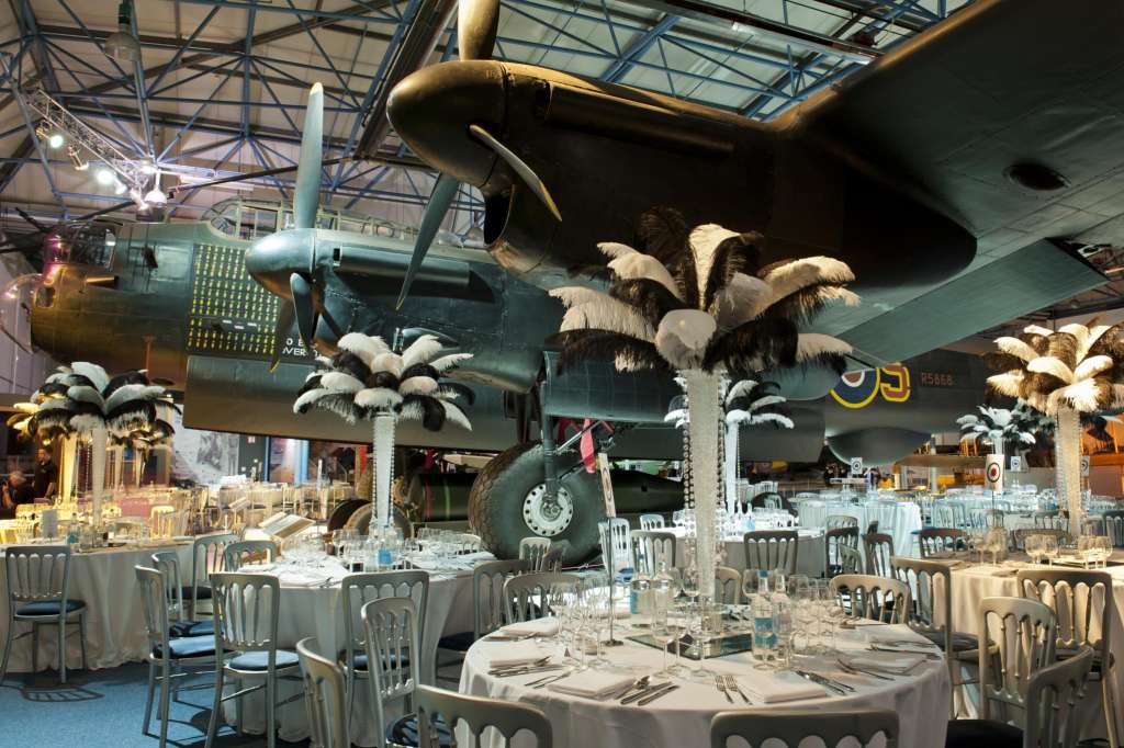 Sunderland Hall set up for a seated dinner with round tables, white linens, and vintage aircraft overhead.
