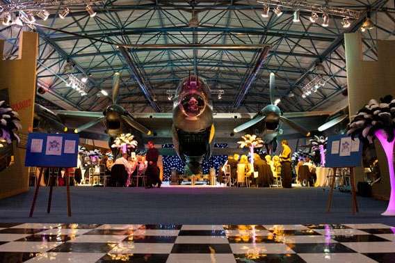 Sunderland Hall set up for an event with aircraft centerpiece, illuminated floral arrangements, and stage lighting.