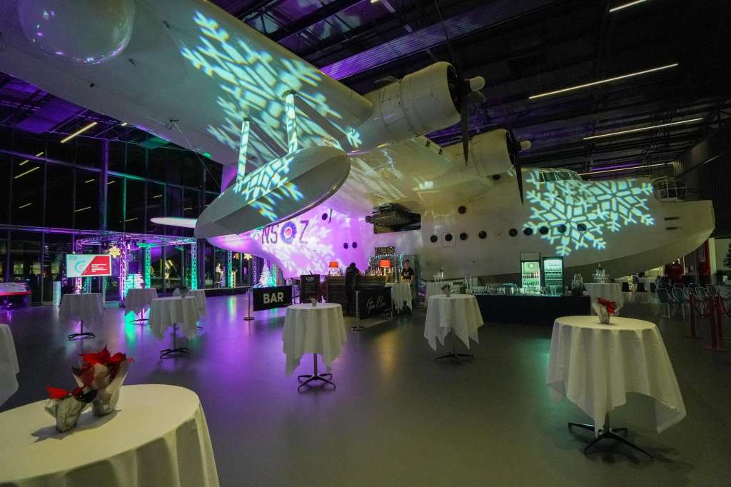 The Sunderland Hall set up for an evening event with cocktail tables, atmospheric purple and green lighting, and a historic aircraft overhead.