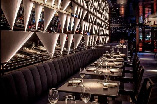 Modern dining room with long tables, place settings, wine glasses, and dramatic geometric wall lighting.