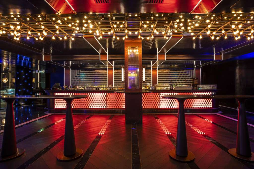 Modern bar interior with red and blue ambient lighting, illuminated ceiling, and geometric bar design.