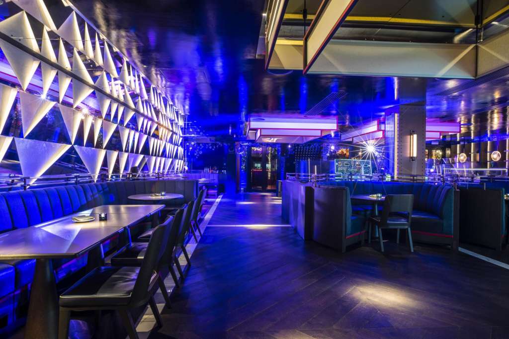 Banquette dining room with blue ambient lighting, geometric wall panels, and modern table settings.