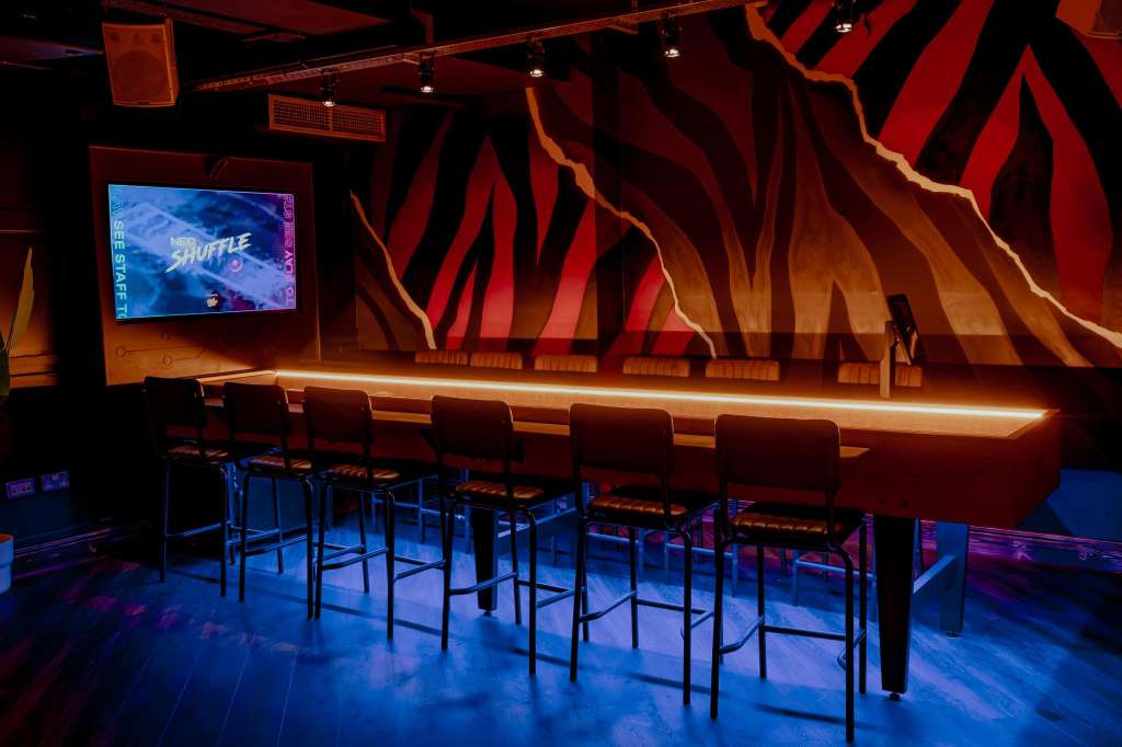 Modern event space with high-top bar seating, dramatic red and orange wall graphics, neon lighting, and large video screen.