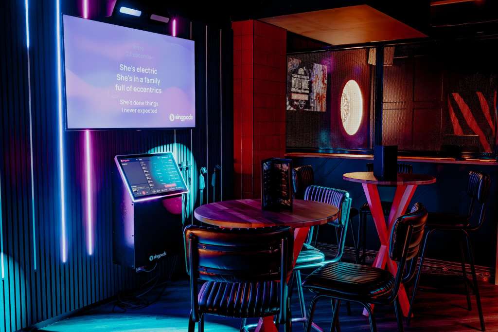 Modern event space with neon lighting, round tables, chairs, projection screen displaying text, and vibrant red and blue decor.