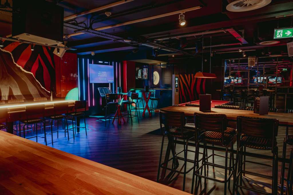 Modern event space with neon lighting, bar seating, high-top tables, and projection screen setup.