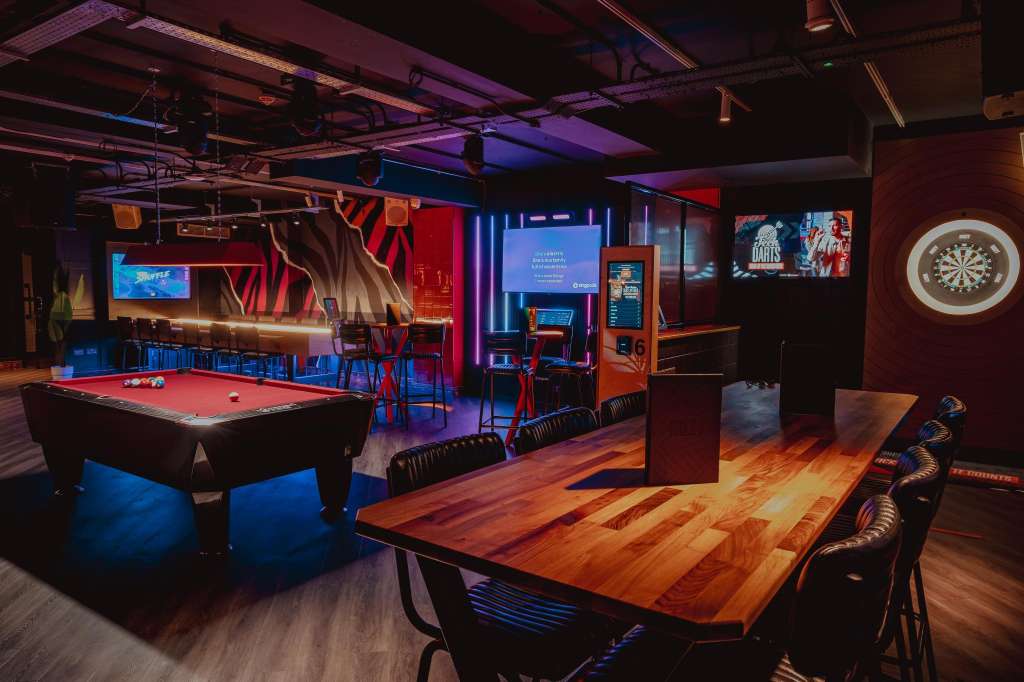 Entertainment space with pool table, arcade games, wooden dining table, and neon lighting throughout.