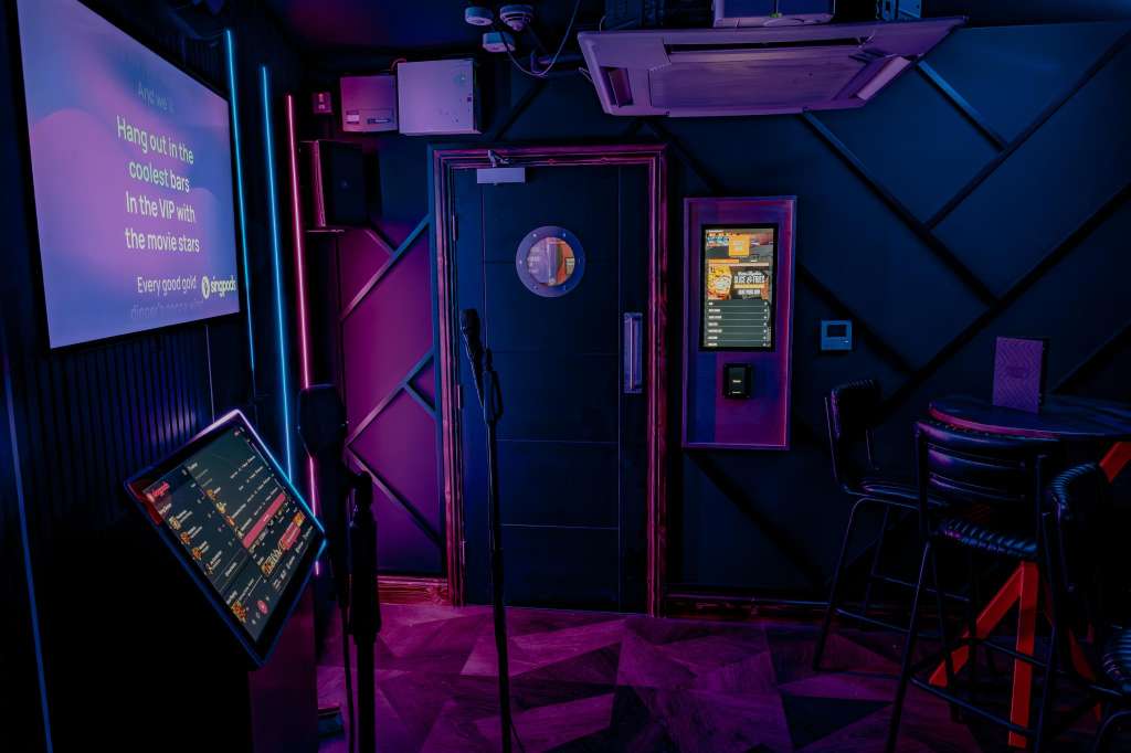 VIP Room with neon-lit bar setup, projection screen, arcade games, and moody purple and blue lighting.