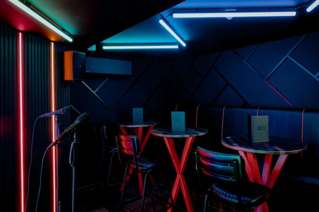 Modern event space with neon lighting, red high-top tables, geometric wall panels, and a microphone setup.