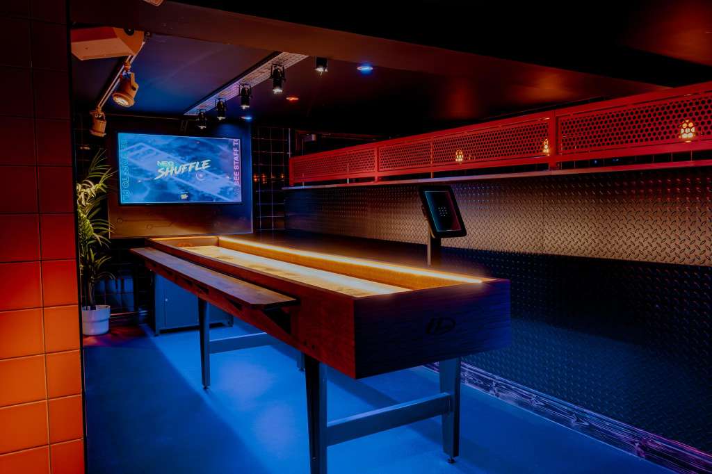Duck pin bowling alley with illuminated lane, scoring screen, and red and blue ambient lighting.