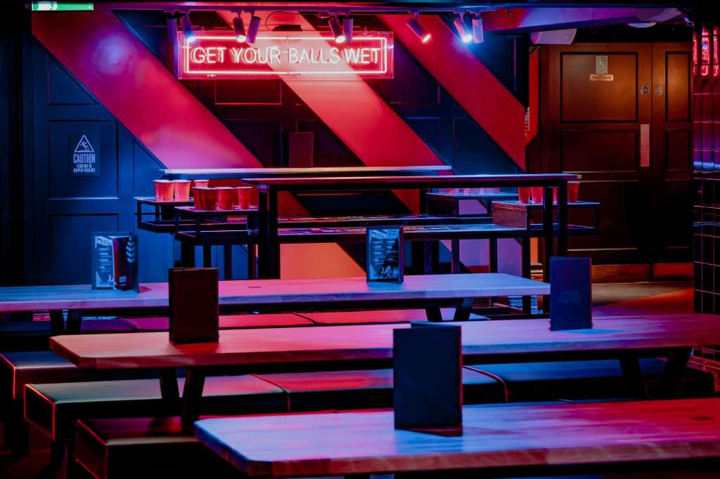 Duck pin bowling alley with neon signage, colorful lighting, and bench seating along lanes.