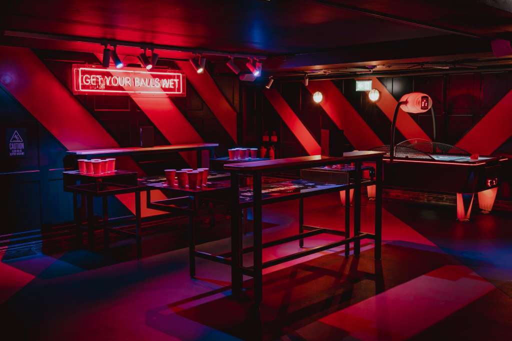 The Bullseye Zone set up for team activities with beer pong tables, neon signage, and red and blue lighting.