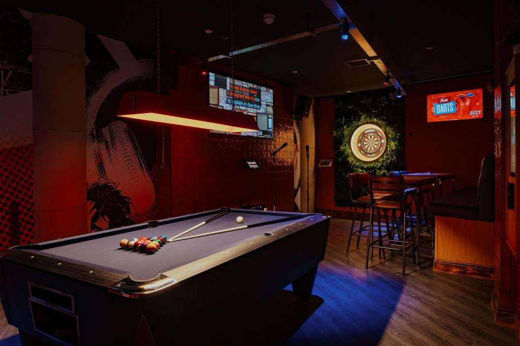 Games room with pool table, dartboard, bar seating, and red ambient lighting.