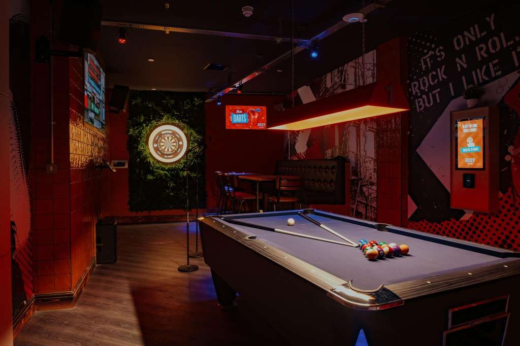 Entertainment space with pool table, dartboard, neon signage, and red ambient lighting. No people visible.