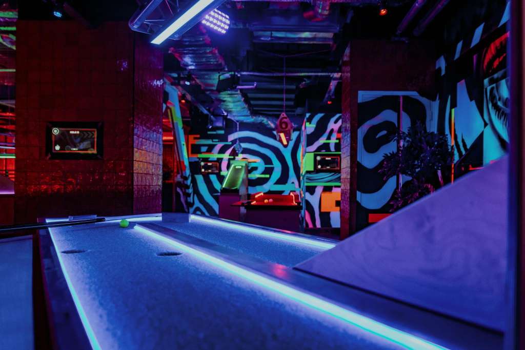 Neon-lit entertainment space with pool table, glowing floor, and colorful graffiti-style wall art.