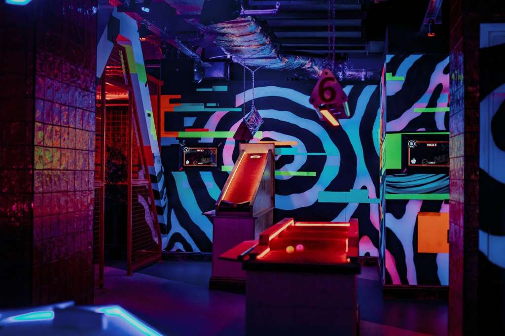 VIP Room with neon-lit games and vibrant geometric wall art in purple, blue, and green lighting.