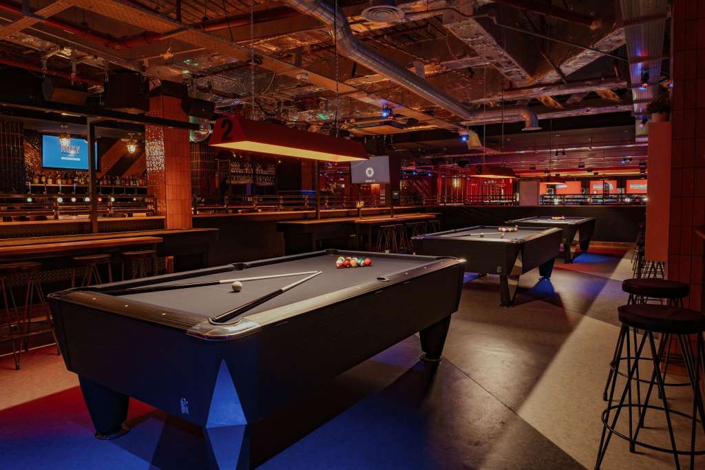 Crazy Pool room with multiple pool tables, bar seating, and ambient red and blue lighting throughout.