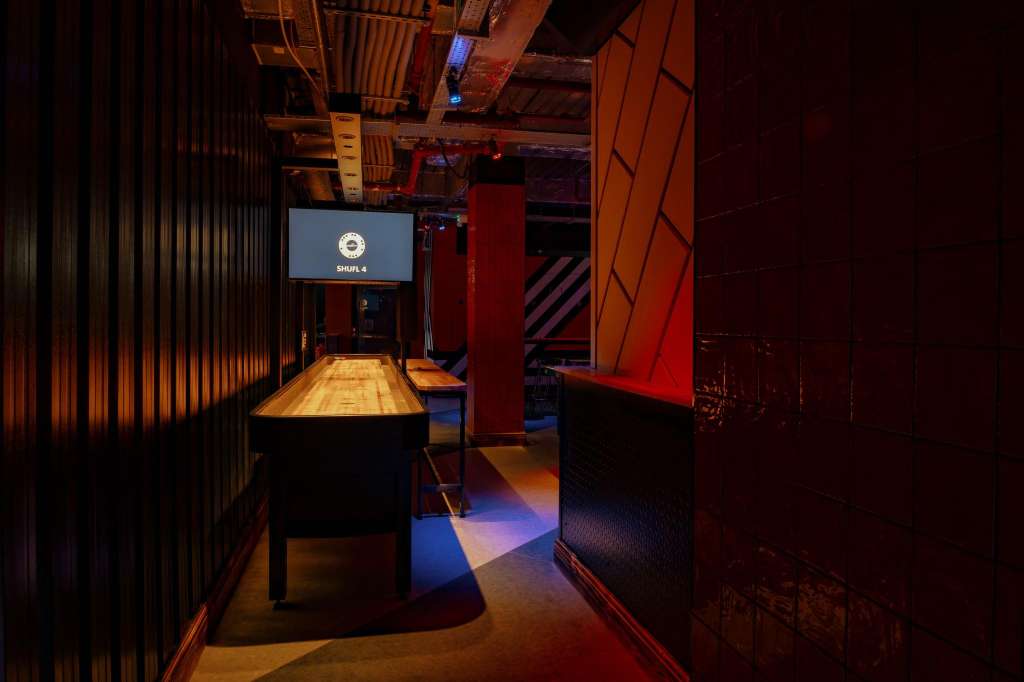 Gaming hall with pool table, colorful floor lighting, red architectural elements, and screen display.