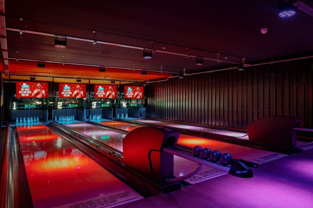 Bowling lanes with neon lighting, scoring displays, and colorful floor illumination in a modern entertainment space.