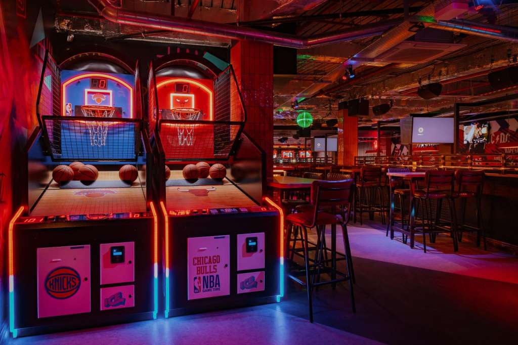 Gaming hall with neon-lit basketball arcade games, bar seating, and colorful LED lighting throughout.