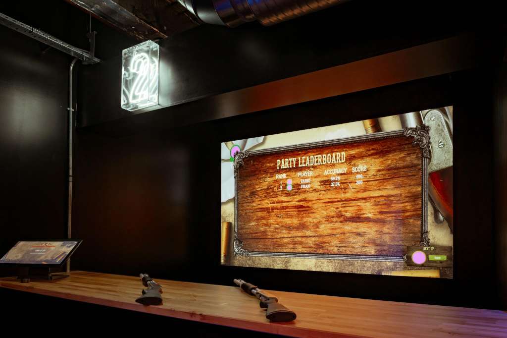 Tournament area with wooden lane, gaming screen displaying party leaderboard, and neon signage overhead.