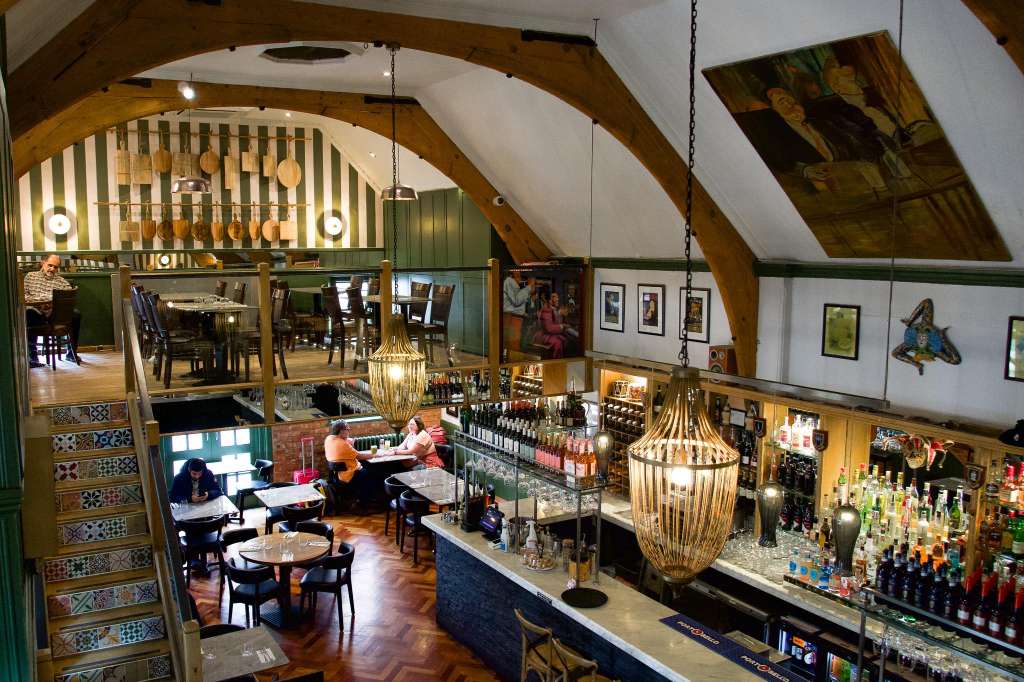 Nonna's Gallery interior with bar counter, pendant lighting, exposed wooden beams, and dining area with guests seated at tables.