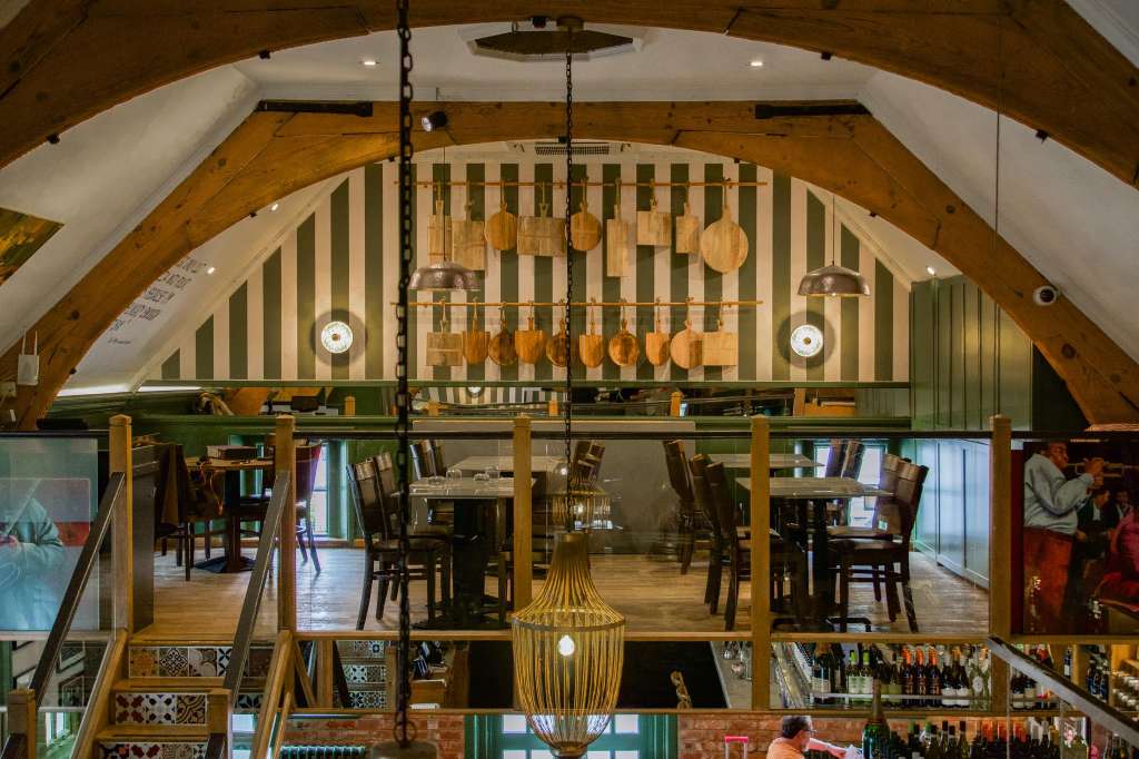 Nonna's Gallery dining space with exposed wooden beams, green and cream striped wall, hanging pendant lights, and wooden chairs at tables.