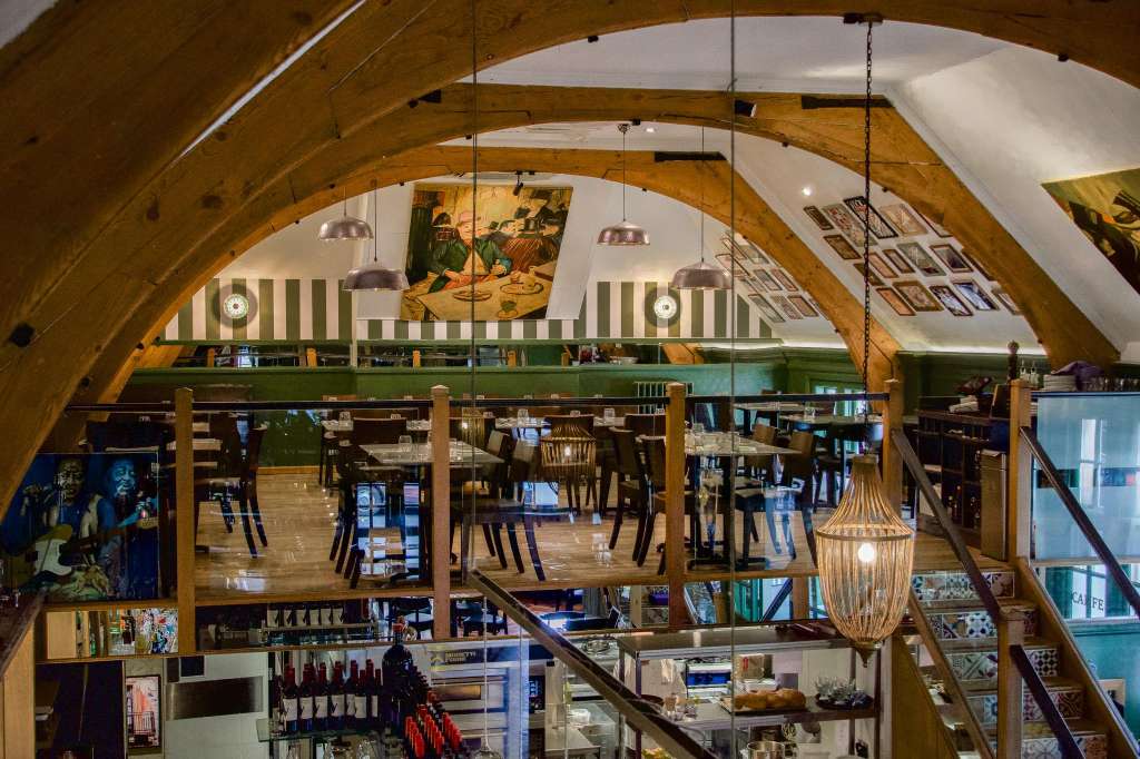 Nonna's Gallery with arched wooden ceiling, pendant lighting, dining tables, and Italian artwork on walls.
