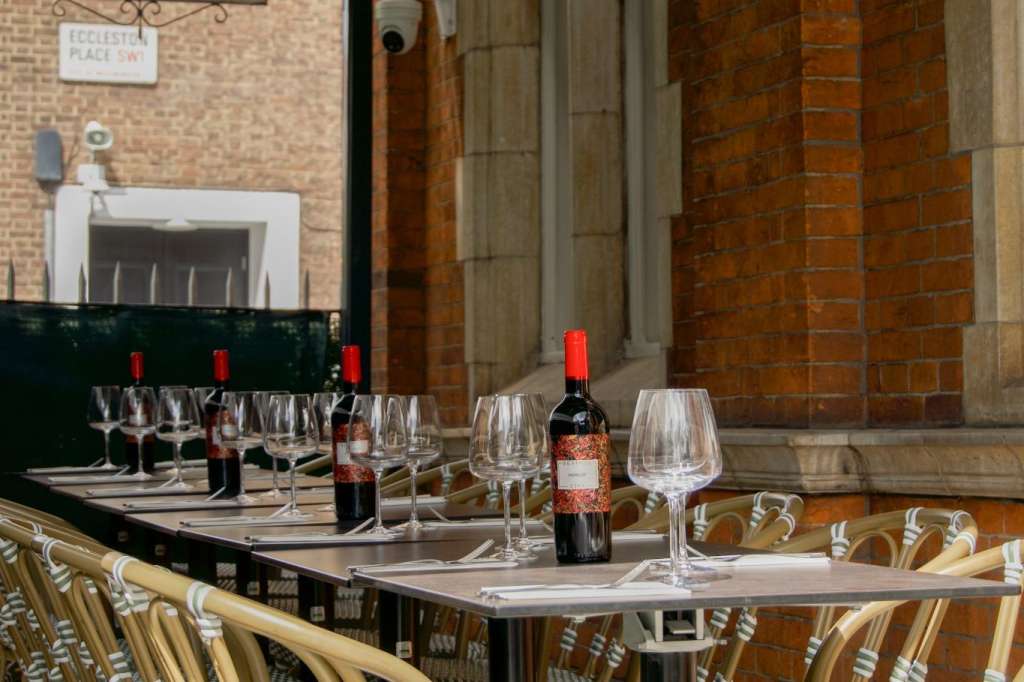 Outdoor dining area with long table set with wine glasses, wine bottles, and red candles. Rattan chairs with striped cushions.