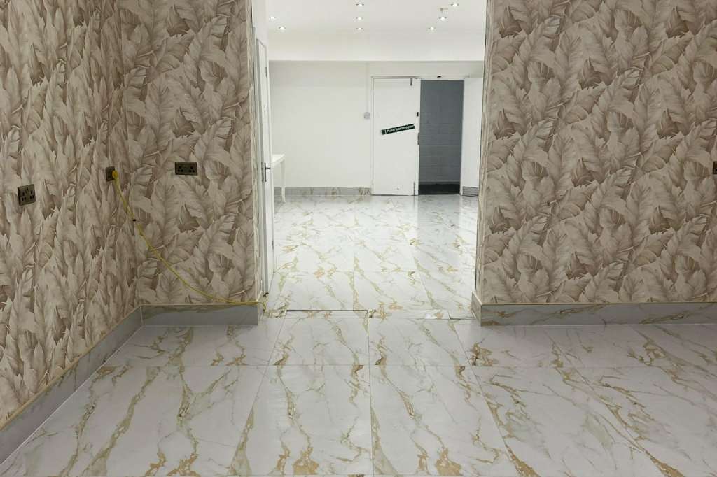 Empty interior room with marble-effect flooring and leaf-patterned wallpaper, viewed through open doorway.