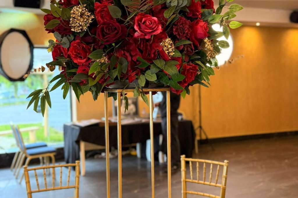 Tall gold vase with deep red roses and greenery centerpiece on black table with candles and place cards.