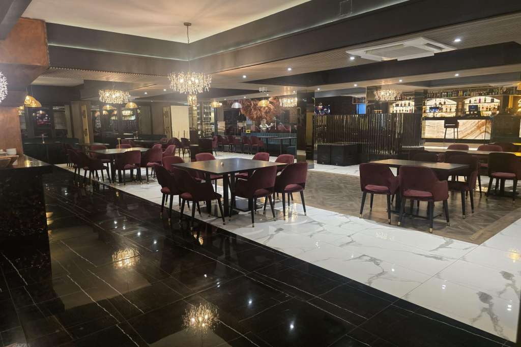 Modern dining space with multiple round tables, burgundy chairs, crystal chandeliers, and bar area with ambient lighting.
