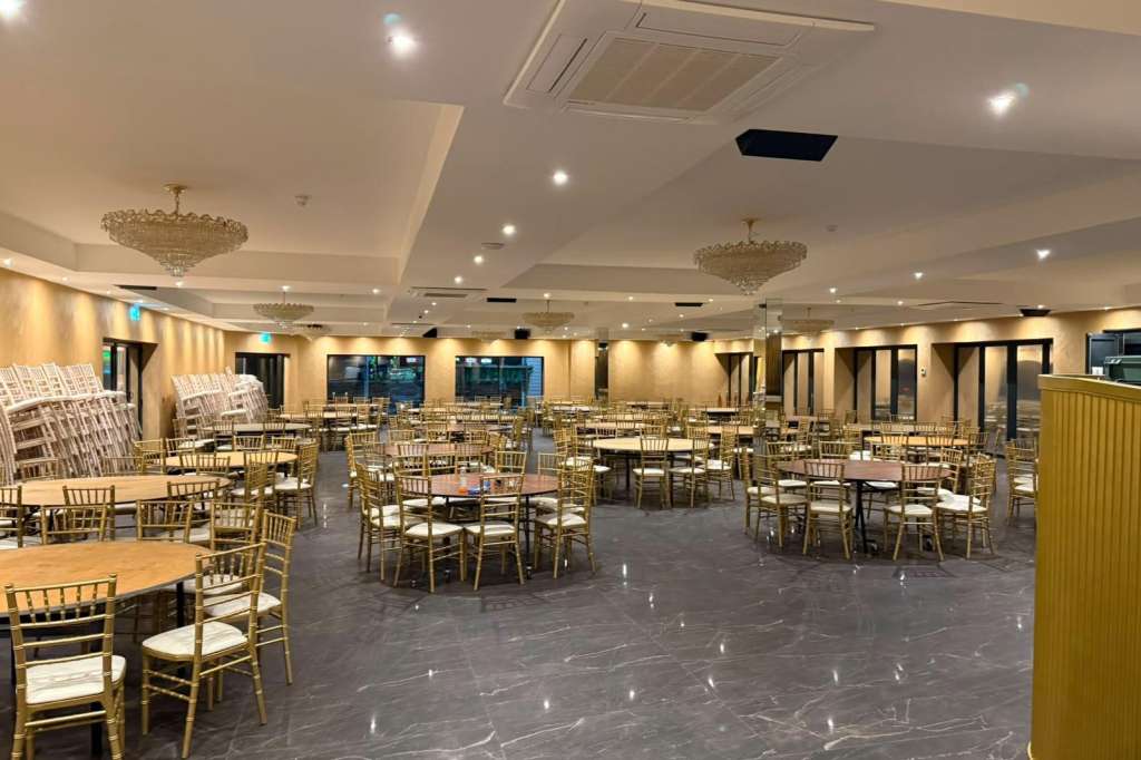 Plaza Suite set with round tables, gold chiavari chairs, crystal chandeliers, and warm ambient lighting.