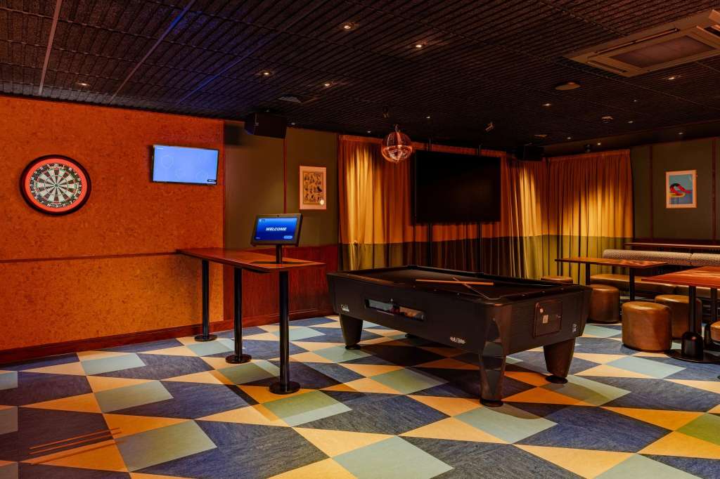The Trophy Room with pool table, dartboard, colorful geometric flooring, orange walls, and entertainment screens.